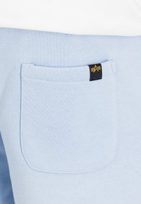 Világoskék szövet, texturált felülettel, hátul egy zsebből áll, amelyet egy fekete címke arany részletekkel díszít.