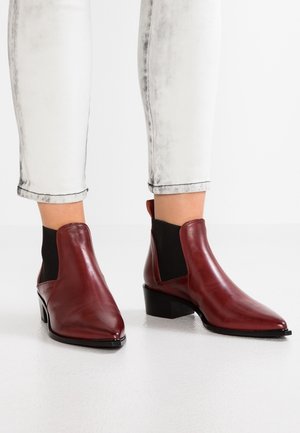 Botines de cuero burdeos con punteras puntiagudas y tacones bajos de bloque, usados con vaqueros de lavado claro remangados.