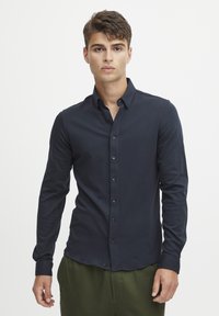 Cămașă albastră închis, cu mânecă lungă, cu nasturi, cu o croială slim. Are un guler clasic și nasturi asortați, fabricată dintr-un material moale și neted.