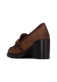 Mocasines de tacón de cuero marrón con puntera redondeada, que presentan un detalle de lazo y un tacón de bloque negro texturizado. Superficie lisa y suela resistente.