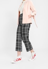 Blazer rose clair à manches retroussées, haut à côtes blanches, pantalon croppé à carreaux noirs et blancs, et baskets blanches avec des accents rouges.