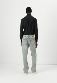 Svart langermet skjorte kombinert med lyseblå, avslappede denimjeans. Jeansene har en lærpatch og et trekantet logo på baklommen.