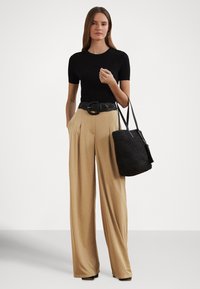 Czarny prążkowany top z krótkim rękawem, beżowe spodnie z szerokimi nogawkami i wysokim stanem, czarny pleciony pasek oraz czarna pleciona torba na ramię. Gładkie tło.