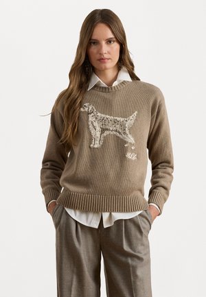 Beige gebreide trui met een geborduurd hondenontwerp. Geribbelde zoom en manchetten, gedragen over een witte blouse met kraag.
