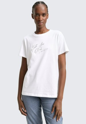 Weißes Baumwoll-T-Shirt mit einem Druckdesign, das "5th Ave Club" in schwarzer Schrift zeigt, kombiniert mit hellblauen Jeans.