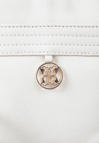 White leather handbag with horizontal stitched accents and a circular gold-tone hardware detail featuring a floral pattern.