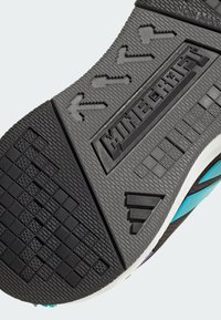 Čierna gumová podrážka topánky má textúrované vzory, vyrazené logo "Minecraft" a dizajn šípok. Akcenty sú v tyrkysovej a bielej farbe.