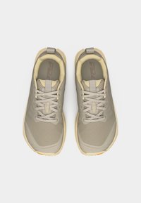 Ζευγάρι αθλητικών παπουτσιών σε μπεζ και γκρι χρώμα με κορδόνια, επενδυμένους γιακάδες και θηλιές για κράτημα, σε θέα από πάνω πάνω σε λευκό φόντο.