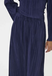 Robe plissée bleu marine avec des manches longues, un corsage ajusté et une taille froncée, mettant en valeur un tissu doux et texturé.
