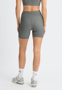 Shorts atletici grigi a coste con una vita alta, che arrivano a metà coscia, abbinati a calzini bianchi e scarpe da corsa. Vista posteriore.