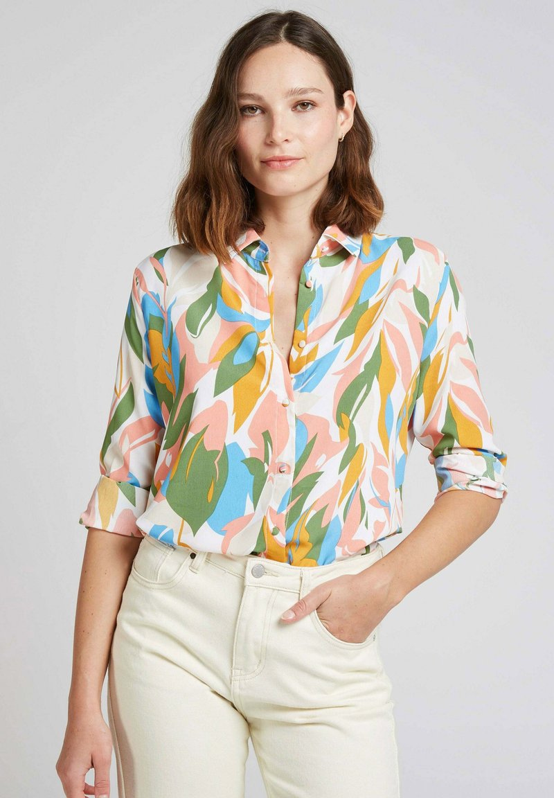 Chemise à manches courtes colorée avec des motifs de feuilles abstraites audacieux en rose, vert, bleu et jaune sur un fond clair ; tissu léger.