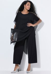 Túnica de gasa negra con mangas anchas y adornos en los hombros, combinada con pantalones de pierna ancha negros y tacones plateados.
