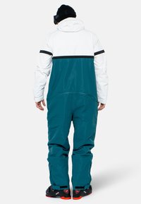 Türkis-weißes Schneeanzug mit lockerem Schnitt, mit einem schwarzen Streifen über dem Rücken und schwarzen Akzenten an den Knöcheln und Schultern.