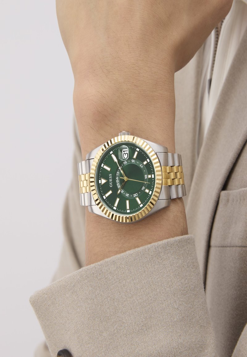 Silver and gold-tone watch with a green dial, date display, luminous hour markers, and a stainless steel bracelet with gold accents.