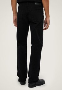 Jeans de denim negro con corte recto, que cuentan con bolsillos traseros, un parche de cuero en la cinturilla y se llevan con botas negras.