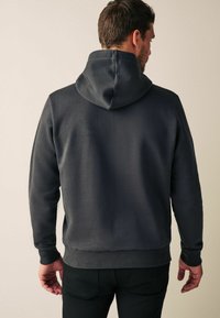 Haut de survêtement gris foncé en tissu doux avec une capuche et des poignets côtelés. Présente une coupe décontractée et une texture lisse. Aucune motif ou logo visible.