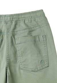 Světlé zelené, měkké kalhoty z látky s elastickým pasem, které mají dvě zadní kapsy a decentní švy.