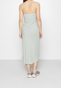 Robe midi vert menthe à pois blancs, avec des bretelles spaghetti et une coupe ample, associée à des chaussures de sport argentées et roses.