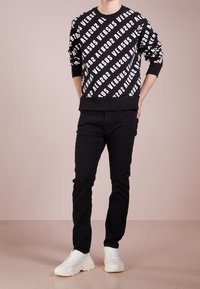 Felpa nera con un audace motivo di testo bianco "VERSUS", polsini e orlo a coste. Abbinata a pantaloni neri slim-fit e sneakers bianche chunky.