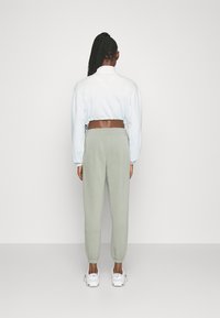 Kort ljusblå sweatshirt med dragsko; kombinerad med ljusgröna joggerbyxor med elastiska uppvik och vita sneakers.