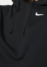 Zwarte hoodie van zachte stof met een kangoeroezak, een capuchon met trekkoord en een wit Nike-logo op de borst. Soepele textuur.