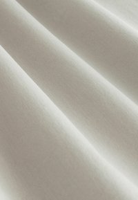 Letvægtsstof med en blød, tekstureret overflade i en neutral beige farve, der har bløde folder og en glat finish.
