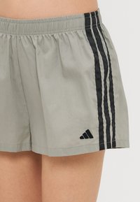 Svijetlosivi atletski šorts s crnim elastičnim pojasom, s tri crne bočne trake i izvezenim logotipom na nozi.