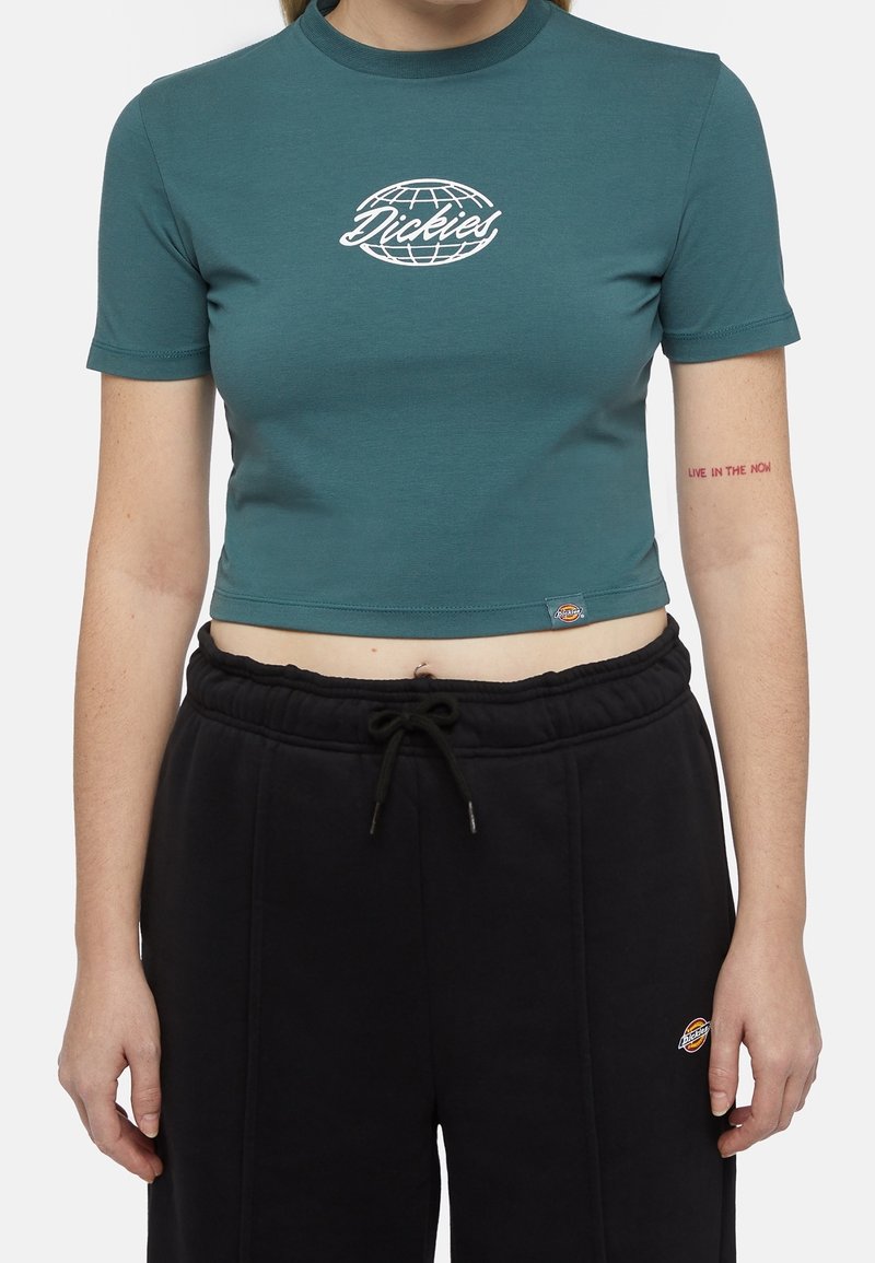 Tyrkysové krátké tričko z měkké bavlny, s bílým logem globu a nápisem "Dickies". Vzhledem ke kombinaci s černými joggery s elastickým pasem.