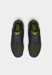 Ζευγάρι σκούρα πράσινα και ναυτικά αθλητικά παπούτσια Reebok με λευκές σόλες, πάνω σε λευκό φόντο, φωτογραφημένα από ψηλά.