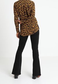 Maglia a maniche lunghe con stampa leopardata in marrone e nero, abbinata a jeans neri a zampa d'elefante. La maglia presenta un orlo arrotondato e una sottile trama.