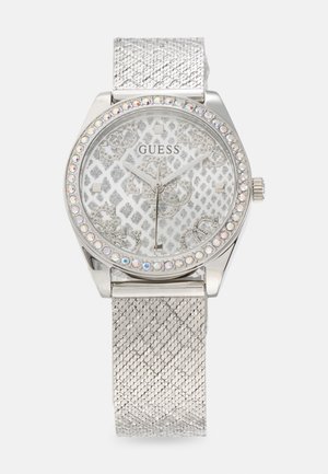 Montre Guess argentée avec un cadran en cristal faceté, un bracelet en maille texturée, et un cadran blanc à motifs avec des accents et des aiguilles argentées.