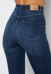 Donkerblauwe high-waisted jeans met een gladde textuur, uitgerust met een leren label bij de tailleband en een klassieke vijf-pocket ontwerp.