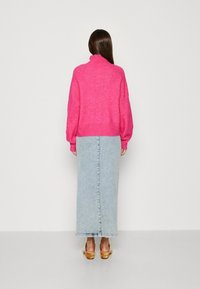 Horká růžová oversized svetr s žebrovaným lemem v kombinaci s maxi sukní z lehkého modrého denimu. Oblečení má rozparek na zádech.