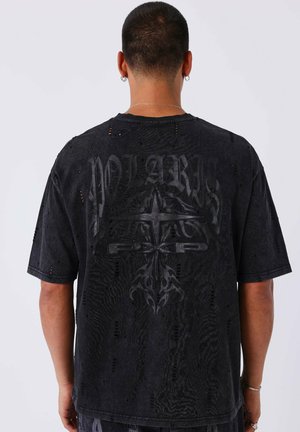 Camiseta negra de gran tamaño con detalles desgastados, con una impresión gráfica y un patrón texturizado en la parte trasera. Mangas cortas y corte relajado.