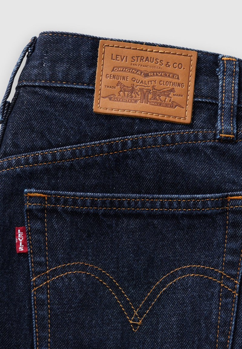Jean en denim bleu foncé avec des coutures orange, un patch en cuir au dos avec un texte de marque, et une petite étiquette rouge Levi's sur la couture latérale.