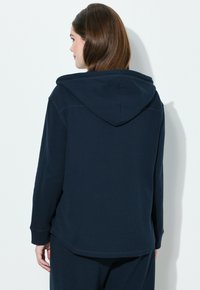 Felpa blu navale realizzata in tessuto testurizzato, con cappuccio regolabile, maniche lunghe e vestibilità rilassata con orlo posteriore leggermente più lungo.