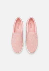 Sapatos slip-on rosas com uma textura suave, colarinho almofadado e sola de borracha branca em contraste; apresentam costuras mínimas e sem atacadores.