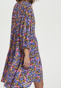 Robe florale avec un fond marine orné de fleurs vibrantes roses, violettes et jaunes. Manches longues avec des poignets froncés et une coupe ample.