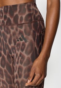Καφέ κολάν με εκτύπωση λεοπάρδαλης, ψηλή μέση, λεία υφή, πλαϊνή τσέπη και μαύρο λογότυπο Adidas στον μηρό.