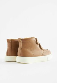 Bottines en cuir marron avec un intérieur doux, dotées d'une sangle en Velcro et d'une semelle en caoutchouc blanc. Texture lisse, design arrondi.