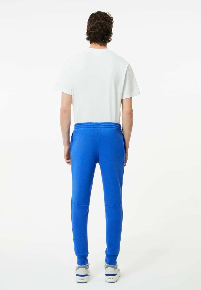 Niebieskie spodnie dresowe z elastycznym pasem i mankietami, w połączeniu z białą koszulką z okrągłym dekoltem i szarymi butami sportowymi.