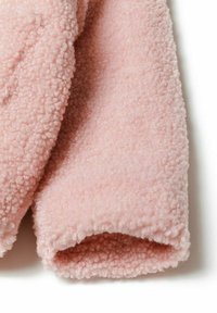 Tessuto di pile rosa con una superficie morbida e testurizzata, con un bordino leggermente arrotolato, che conferisce un aspetto accogliente e caldo.