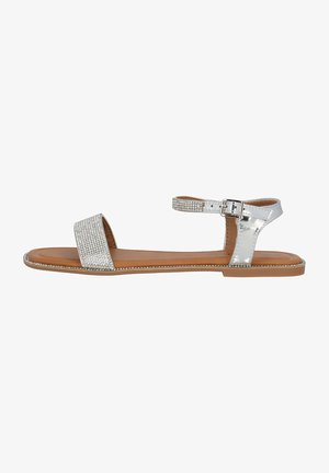 Silver metallic sandal with wide front strap featuring rhinestone embellishments, adjustable ankle strap, and flat brown sole.