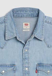 Ανοιχτό μπλε πουκάμισο από τζιν με μυτερό «γιάκετ», κουμπιά τύπου κλιπ και τσέπη στο στήθος. Η ετικέτα γράφει "Levi's", μέγεθος μέτριο, με σχεδιασμό κανονικής εφαρμογής.