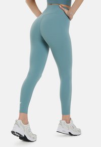 Leggings celestes de tiro alto con una textura suave, que presentan un ajuste ceñido y un sutil logotipo en el tobillo. Combinados con zapatillas deportivas blancas.