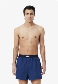 Navy blue cotton boxers with a button front, elastic waistband featuring white logo, smooth texture, and relaxed fit.