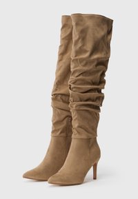 Stivali in suede beige al ginocchio con design arricciato, punta appuntita e sottile tacco a stiletto. Presentano una cerniera all'interno.