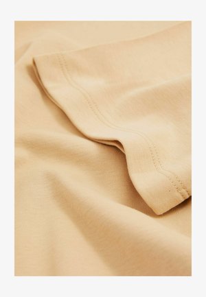 Beżowa tkanina bawełniana o gładkiej fakturze, z subtelnymi detalami w formie prążków i nachodzącym zgięciem. Widoczne są stębnowane krawędzie.
