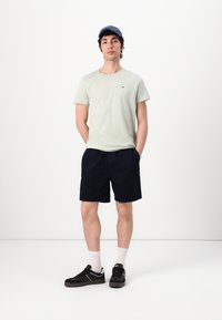 Ljusgrön kortärmad t-shirt, marinblå shorts, vita strumpor och svarta sneakers. Inkluderar en marinblå keps och en liten logodetalj på t-shirten.