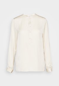 Blusa a maniche lunghe di colore crema in tessuto liscio. Presenta un collo rotondo, una placca frontale con bottoni e polsini con bottoni. Design semplice.